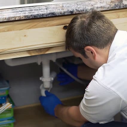 One of our Buffalo plumbers reaches under the kitchen sink to remove a piece of PVC drain pipe.