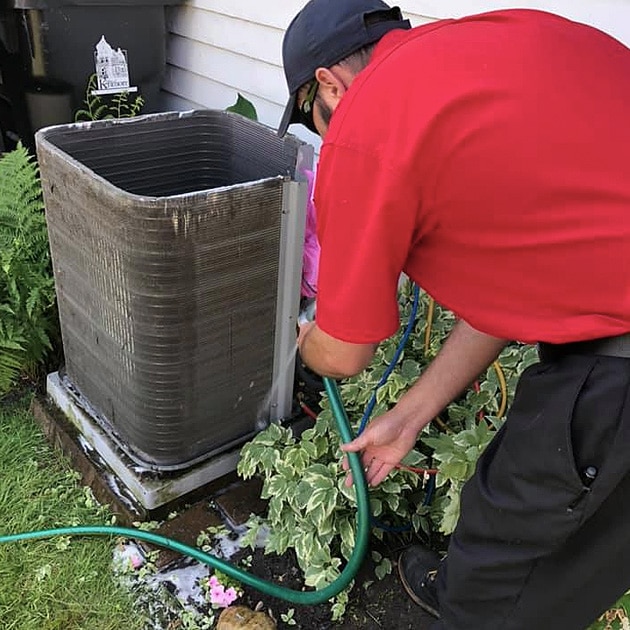 A Reimer technician uses a hose to clean the outside of an AC unit here in Buffalo, NY.