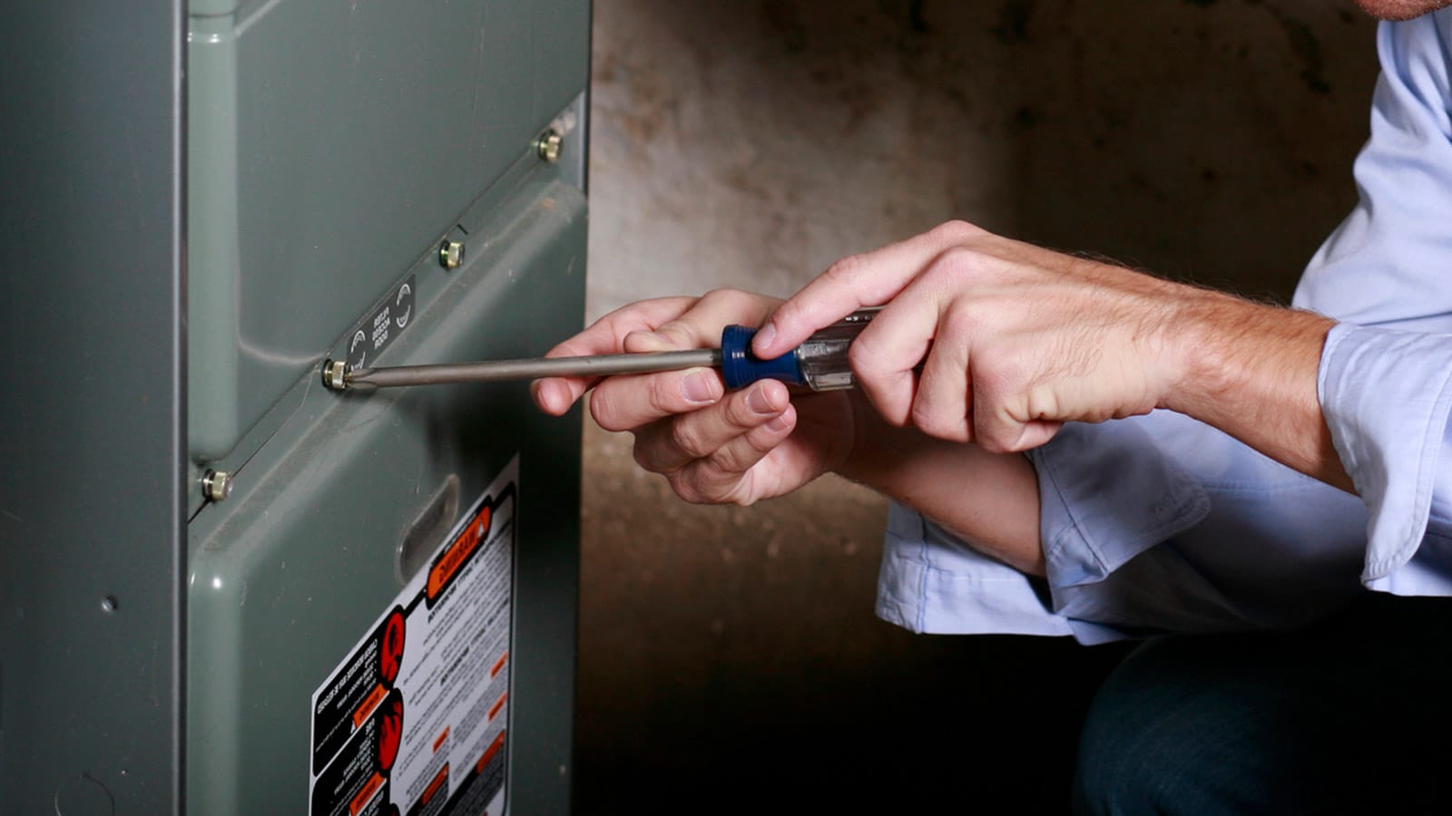 Our plumber uses a screwdriver to attach the faceplate of this gas furnace, completing its installation.