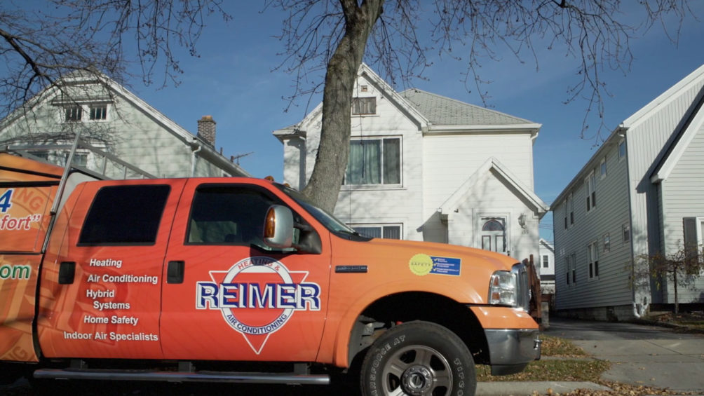 A Reimer service truck pulls up in front of a Buffalo home, with its tech ready to start on HVAC repairs.