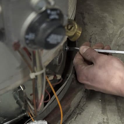 A Reimer plumber uses a flathead screendriver to remove a part from a water heater as part of a repair job.