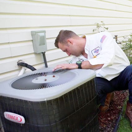 A Reimer technician in a white shirt, blue pants, and work boots fixes a local home's air conditioner here in Buffalo, NY.