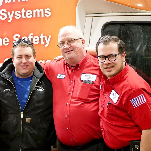 Three of our plumbers pose for a picture in front of our famous orange service vehicle.