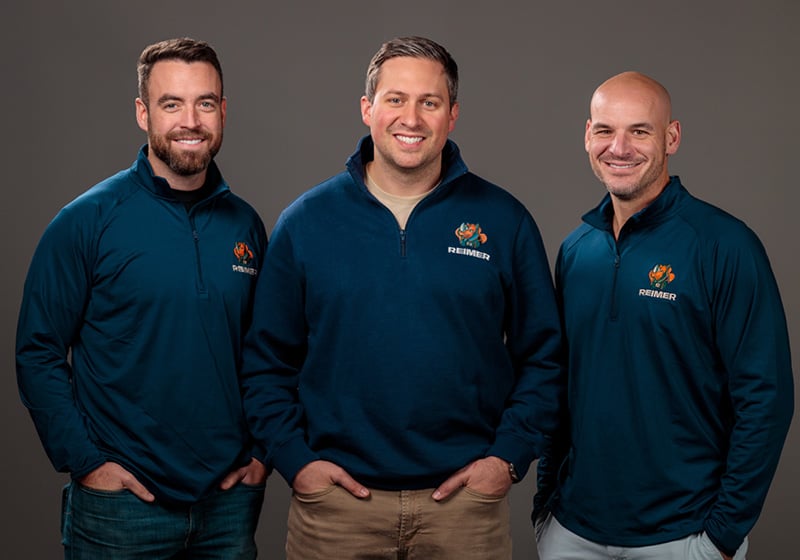 Three of our plumbers pose for a picture in front of our famous orange service vehicle.