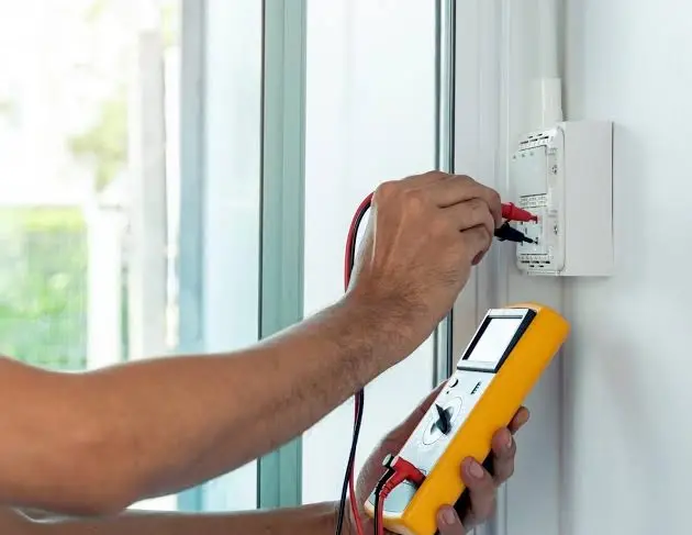 An electrician with a testing tool is carrying out an electrical safety inspection